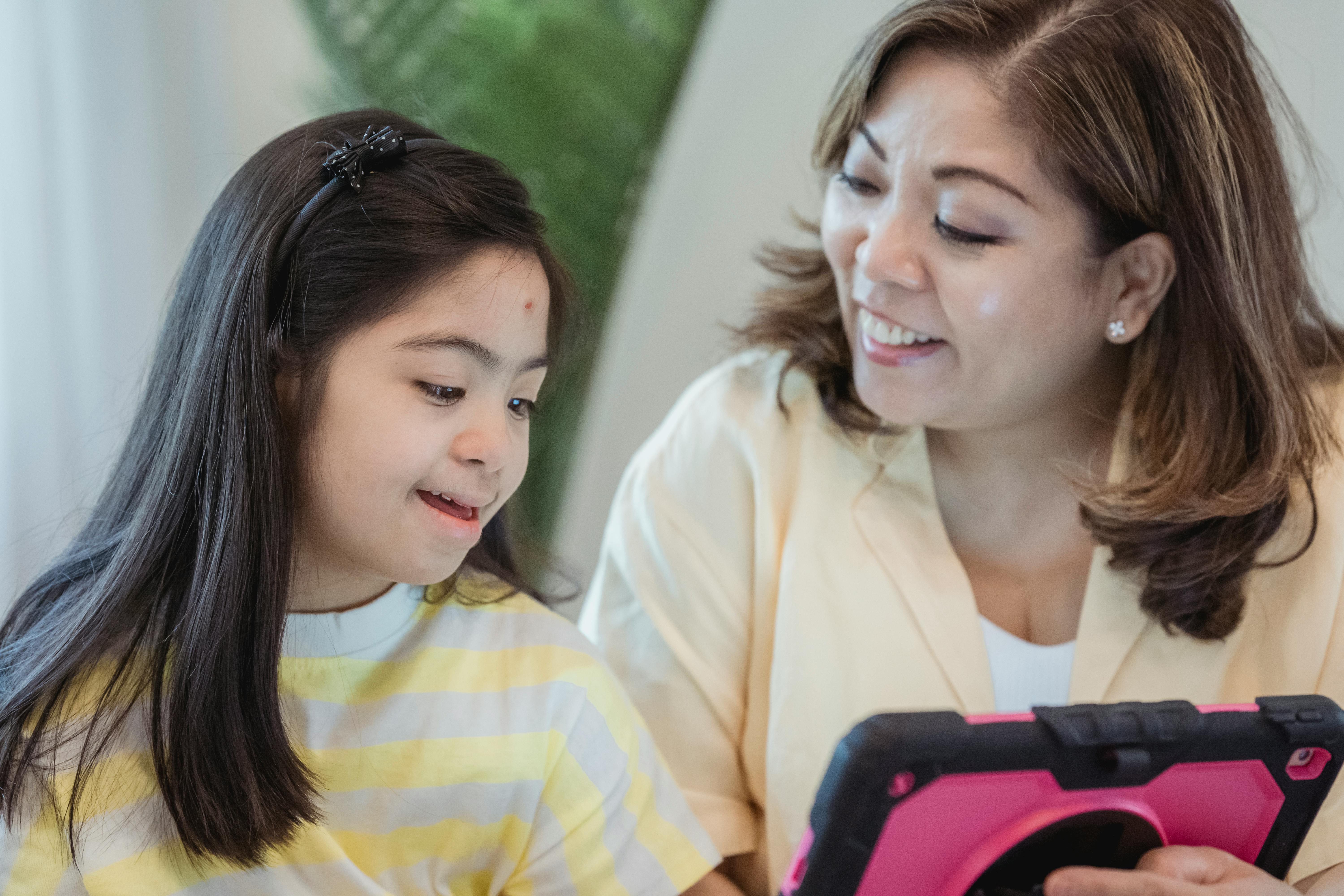 A caregiver and child smiling while using a tablet together