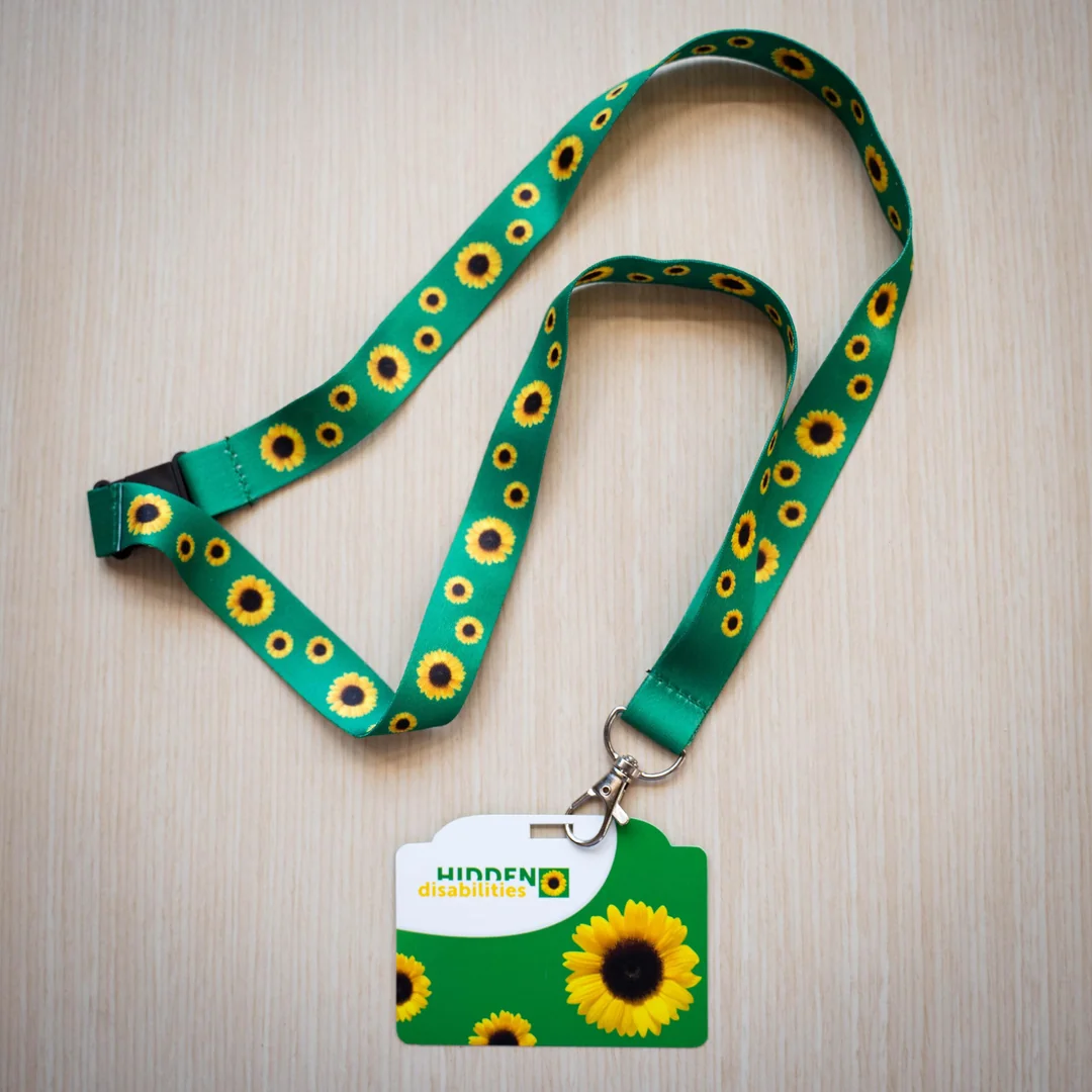 Green sunflower lanyard and Hidden Disabilities ID card on a wooden surface